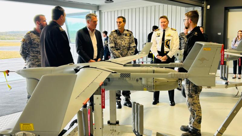 Several men, some in uniform, gather near a small uncrewed aircraft.