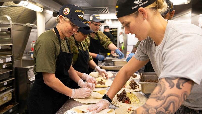 A small group of people prepare food in the kitchen of a ship.