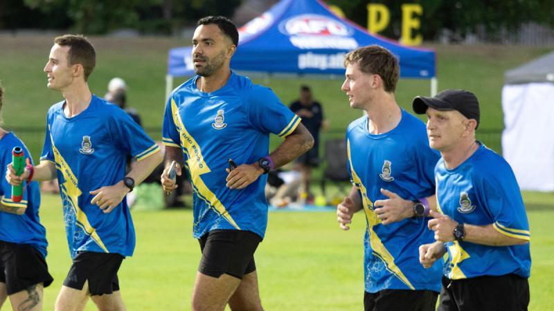 People in blue shirts jogging on an oval.