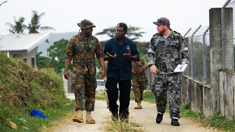Two military men and a civilian walk down a path together, talking.