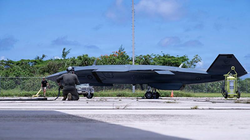 A small aircraft on a tarmac with a person kneeling in front of it.