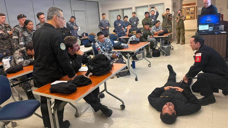 Defence personnel demonstrate a medical procedure to a room full of others.