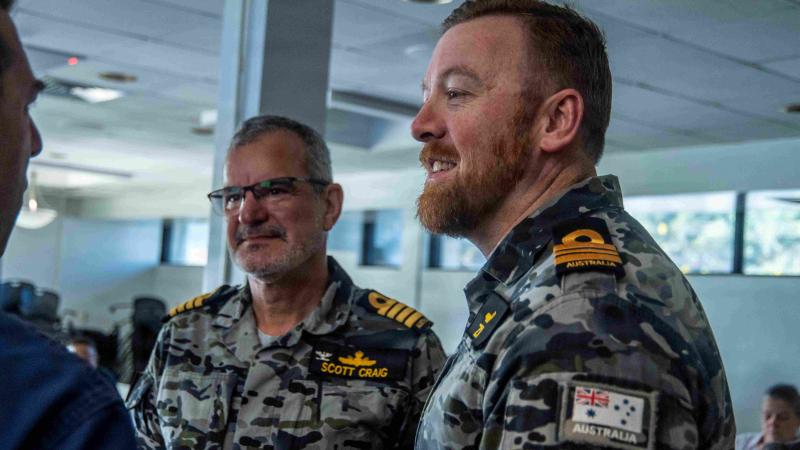 Two men in Australian Navy uniforms stand talking to another.