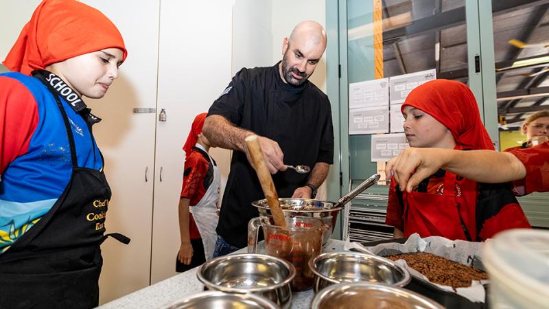 A man helps young children bake with a chocolate mixture.