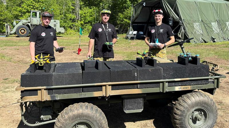 Three Defence members stand behind a trailer which has their drones resting on top.