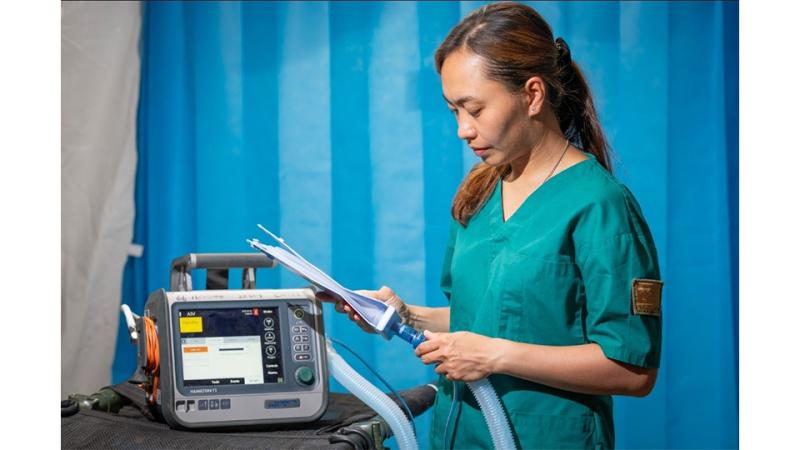 A woman in scrubs inspects a medical device.