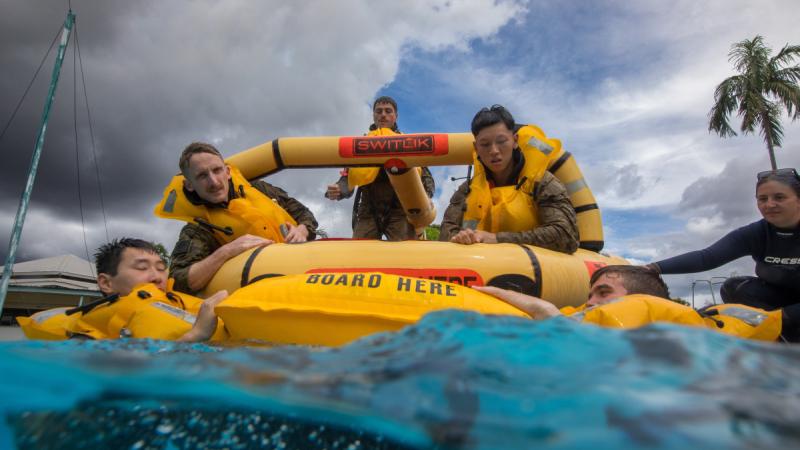 Four soldiers in life vests clamber onto a life raft
