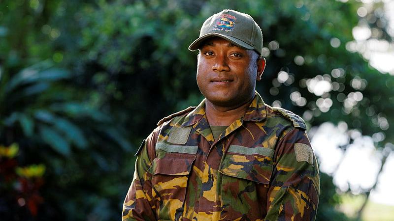 A man in a military uniform poses for a photo outdoors.