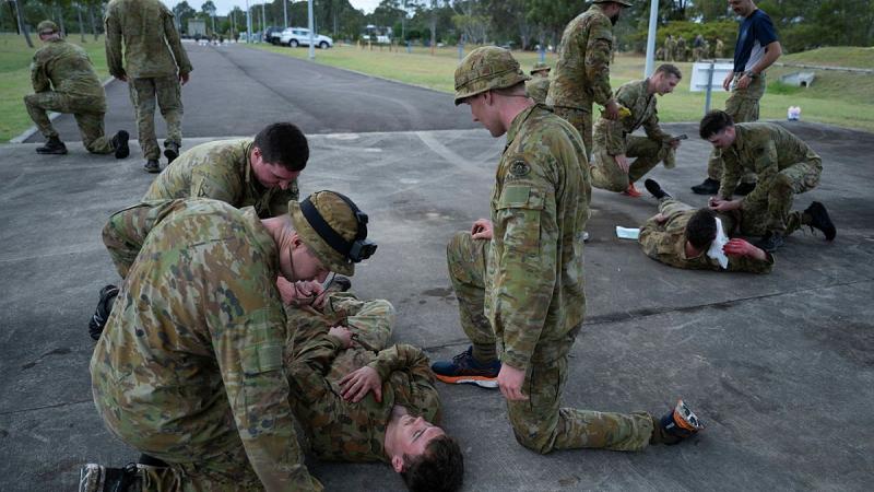 Soldiers gather around a mock patient in an open area.