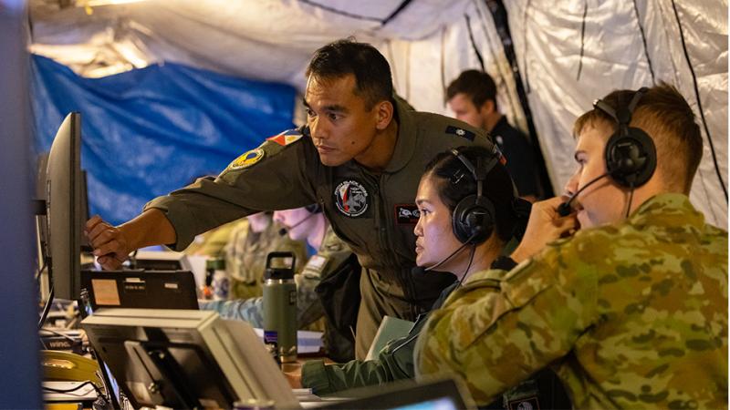 Three military members work on a shared computer.