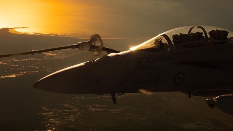 An aircraft flies above a coastal area at sunrise.