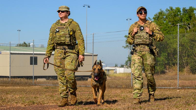 Two military women lead a working dog around a base.
