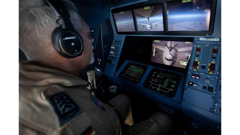 A military member looks at several screens of aircraft in flight.