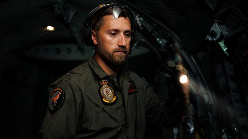 A military man searches around with a torch in the dark.
