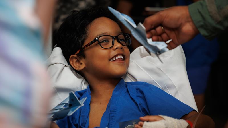A young boy smiles at a miniature aircraft waved in the air.