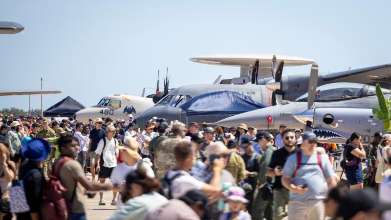A crowd of people walk among small aircraft outdoors.