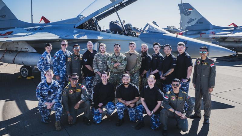 People in different military uniforms stand in front of a jet aircraft.