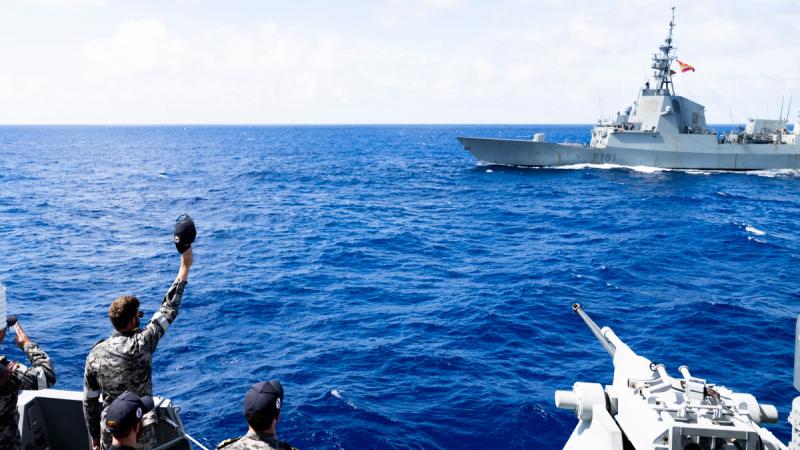 A sailor waves his hat to a passing ship from the deck of another ship.