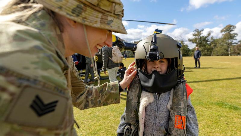 A soldier helps a small child put a helmet on.