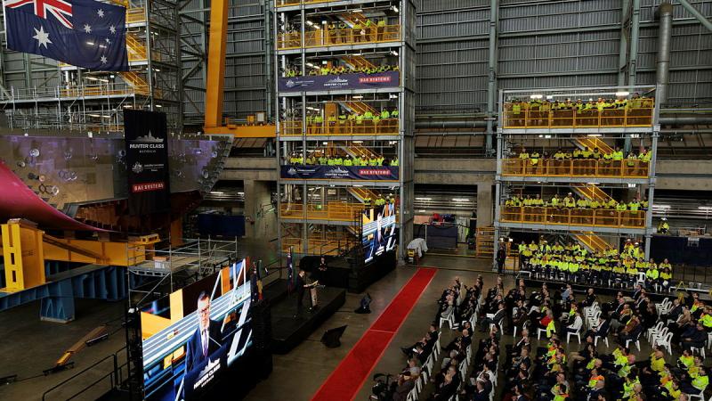A room full of people in high-vis vests listen to a speaker.