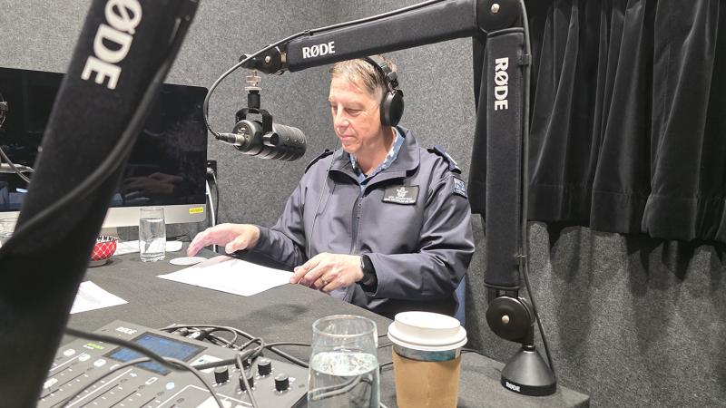 A man speaking into a microphone in a radio recording studio.