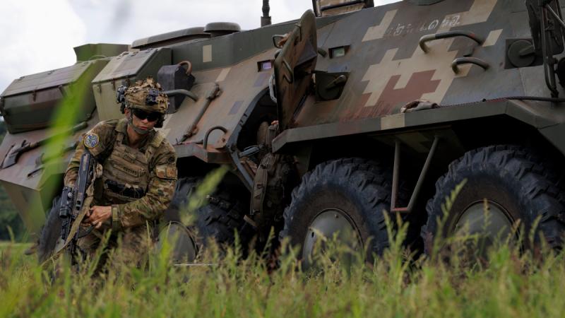 An Army soldier jumps from a truck onto the grass.