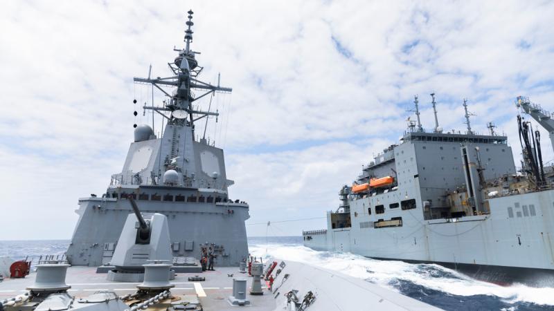 Two navy ships cruise side by side and exchange goods.