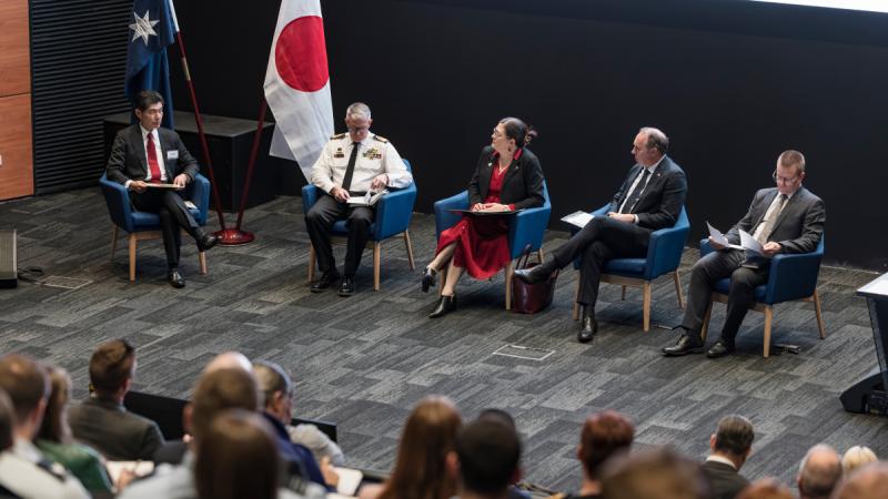 A group of panel members seated on a stage in a lecture theatre.