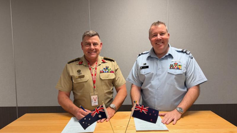 Two men sitting behind a desk signing pieces of paper.