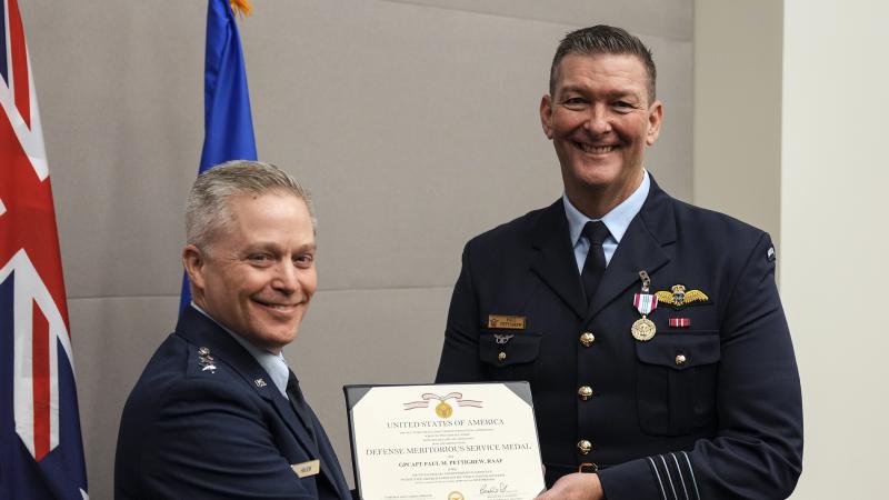 Two men shake hands while holding a certificate between them.