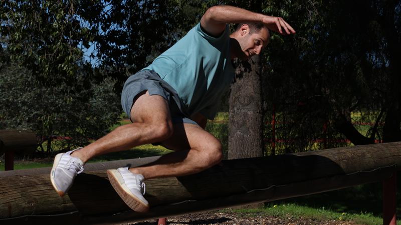 A man leaps over a suspended tree trunk.