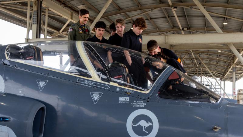 A man in uniform and several teenagers look at the cockpit of an aircraft.
