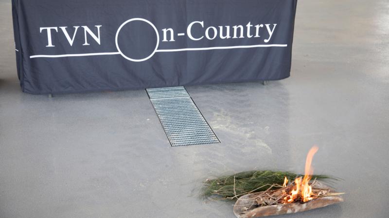 A small piece of bark and leaves are on the ground burning during a smoking ceremony.