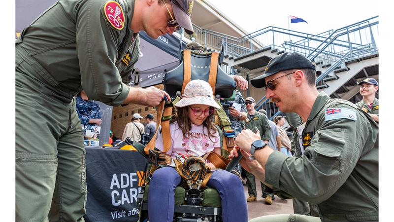 Two military personnel strap a girl into a chair.