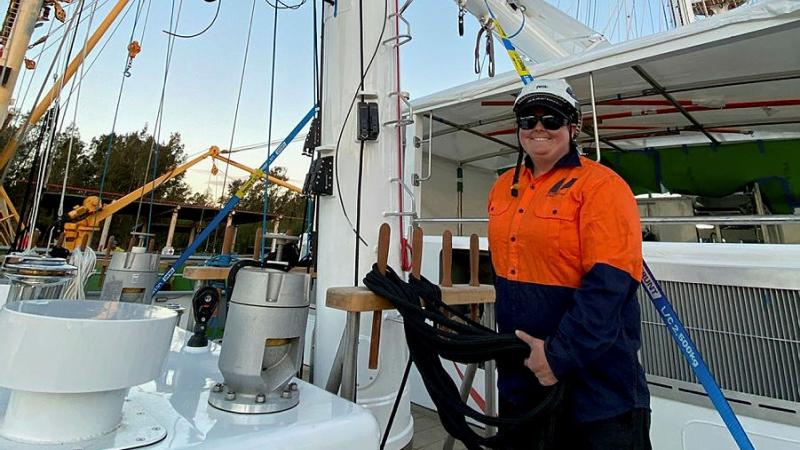 A smiling person stands on the deck of a small ship.