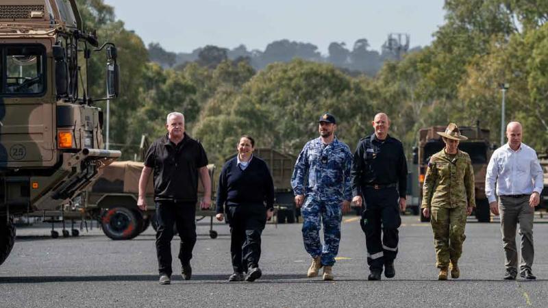 A small group of civilian and uniformed people walk in a line down a base road.